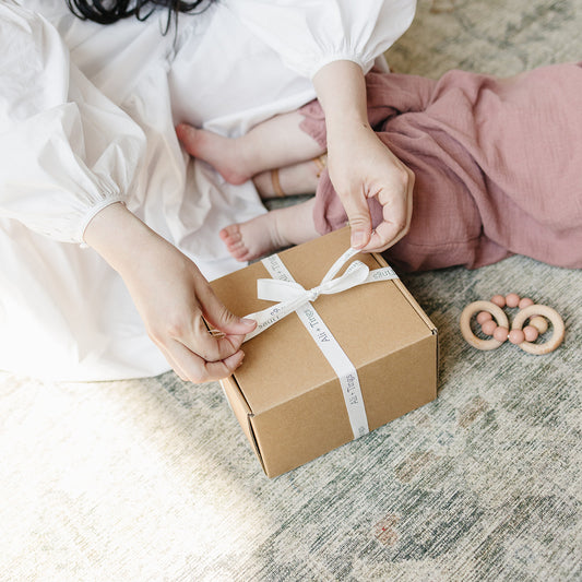 Person tying a ribbon on a cardboard box with a baby in the background