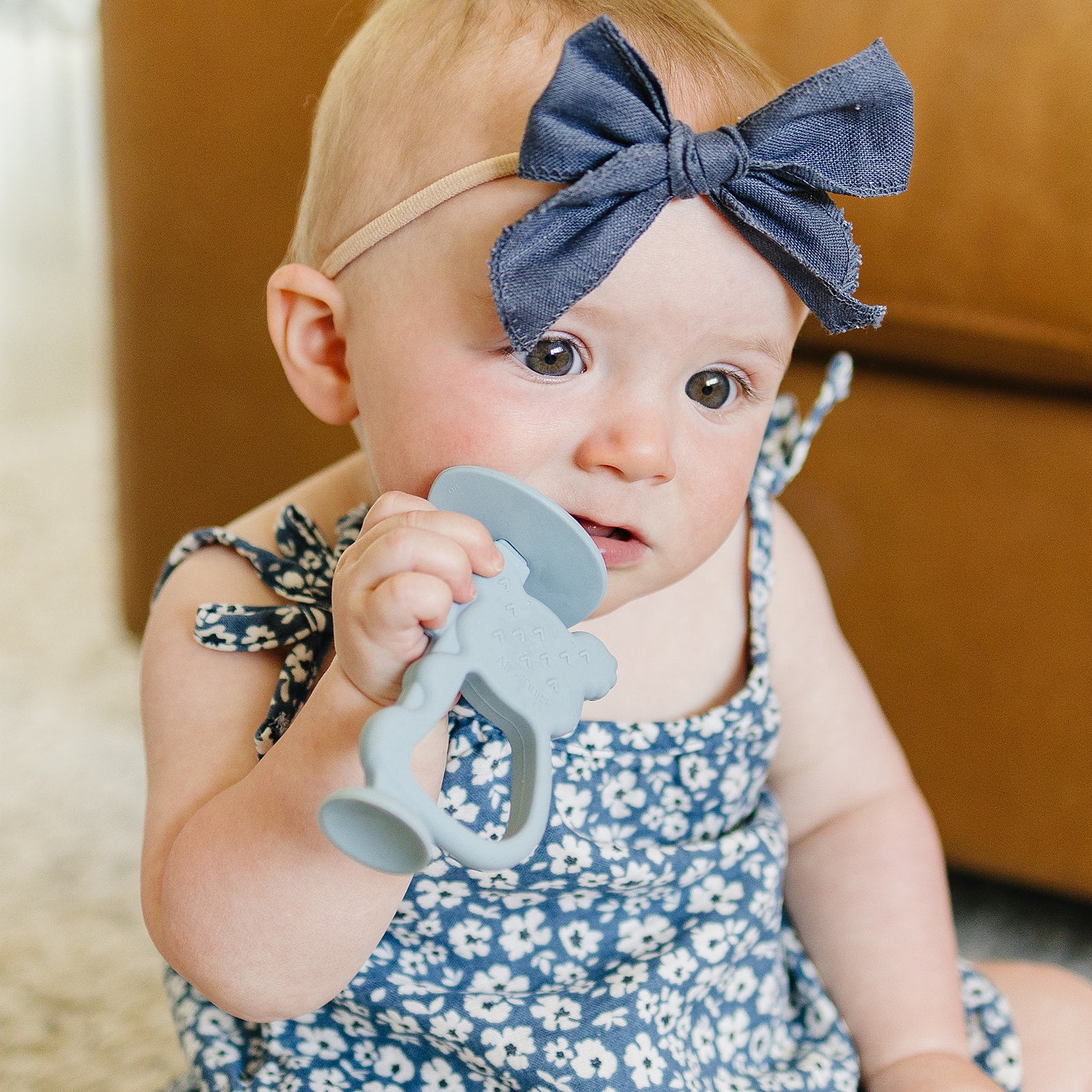Baby holding a blue teething toy with a blurred background