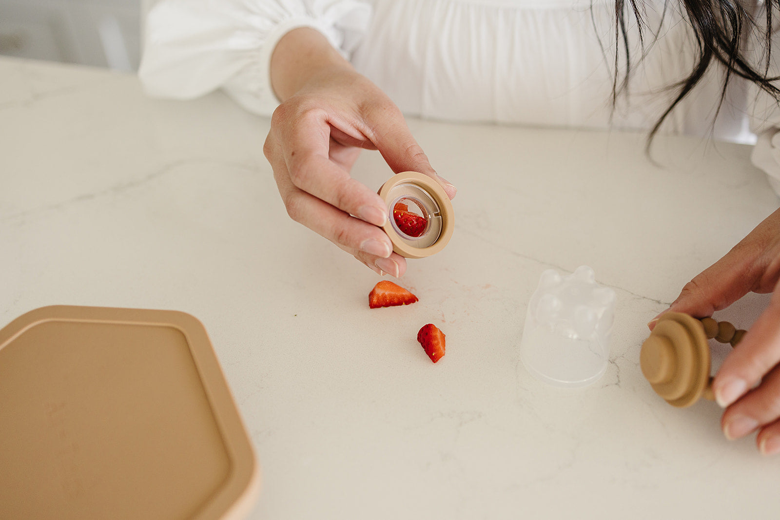 Person pouring strawberries from a wooden container onto a white surface