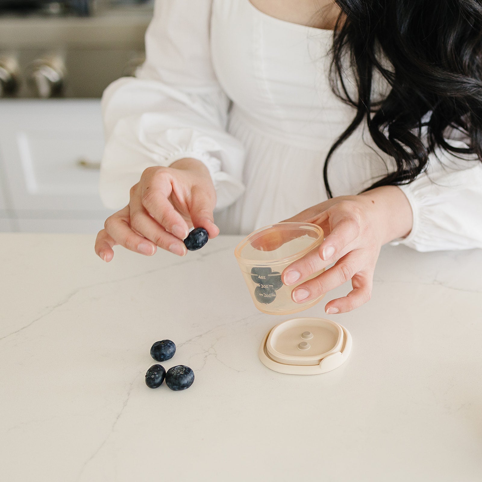 Person holding a small container with blueberries on a kitchen counter