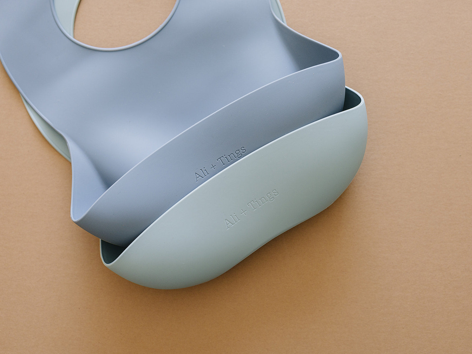 Two light blue silicon bibs stacked on a beige background
