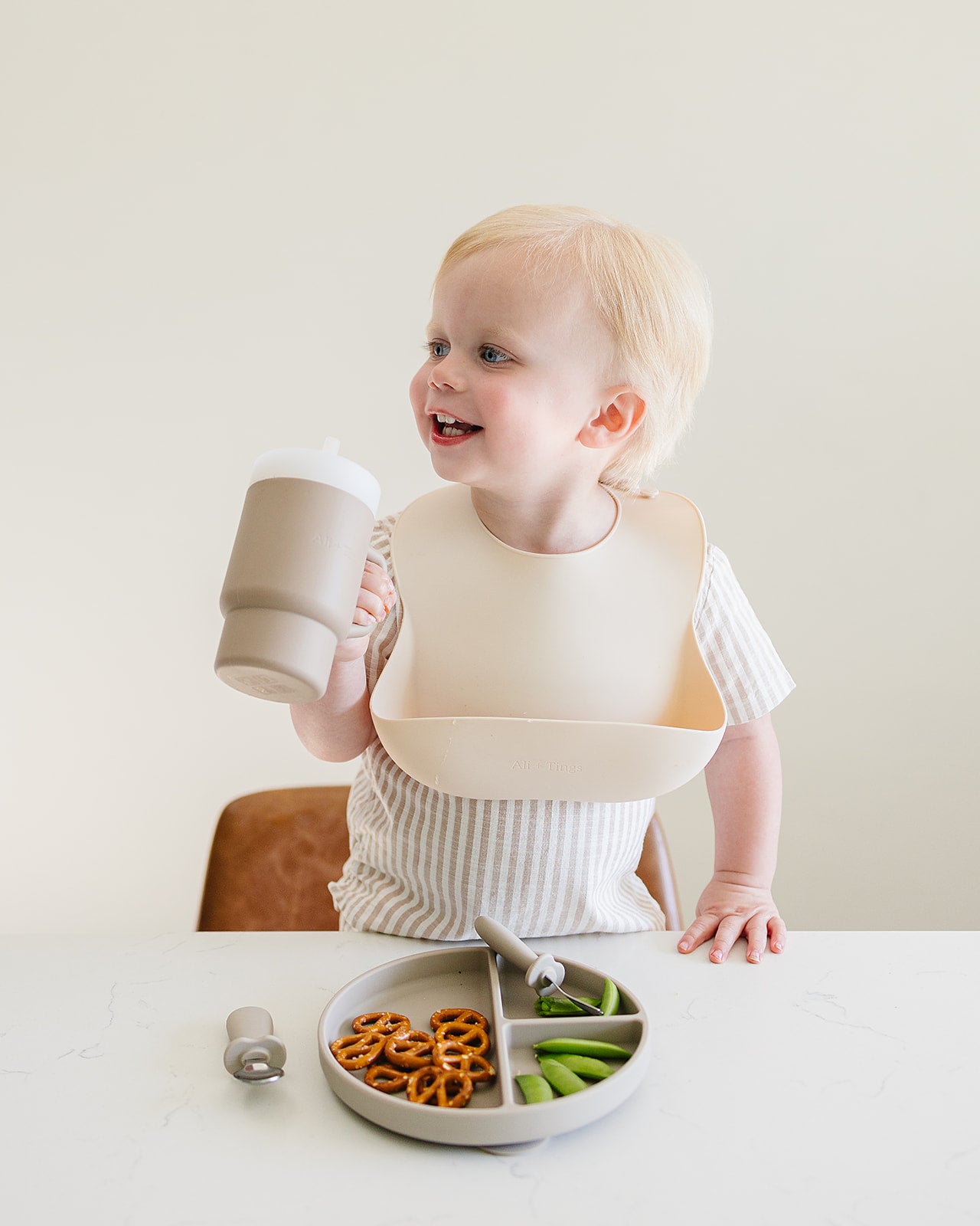 Child wearing silicone bib holding and holding soft silicone tumbler for babies in neutral color