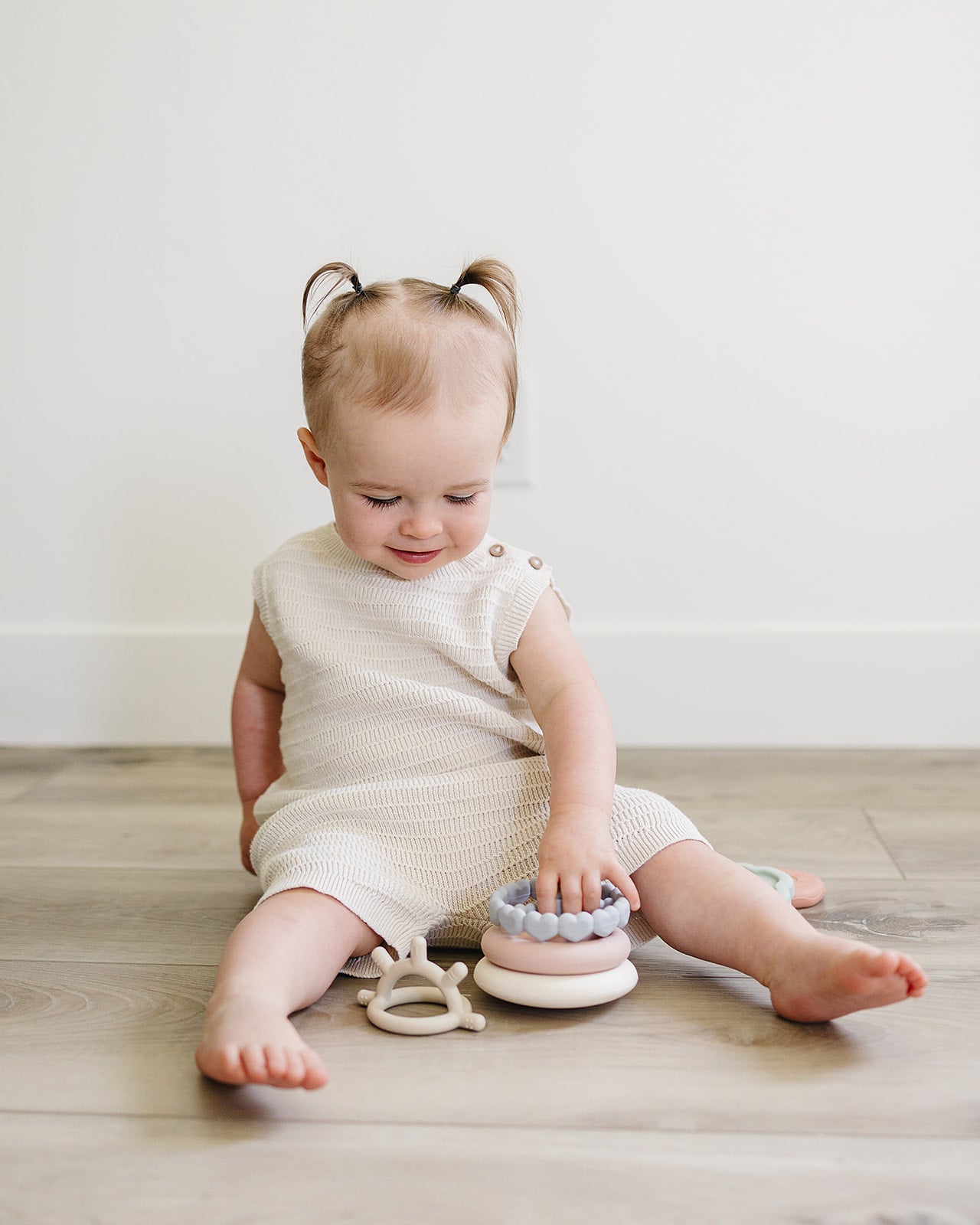 Baby sitting on a wooden floor with colorful stacking toys