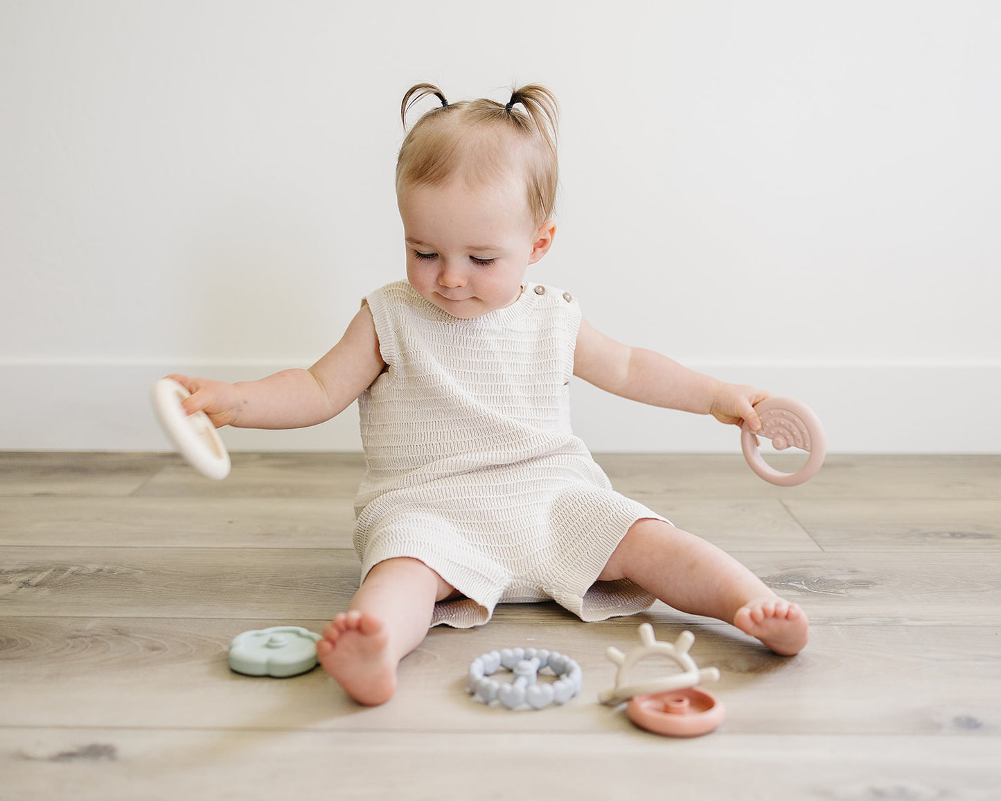 Young child sitting on a wooden floor with various teething toys around