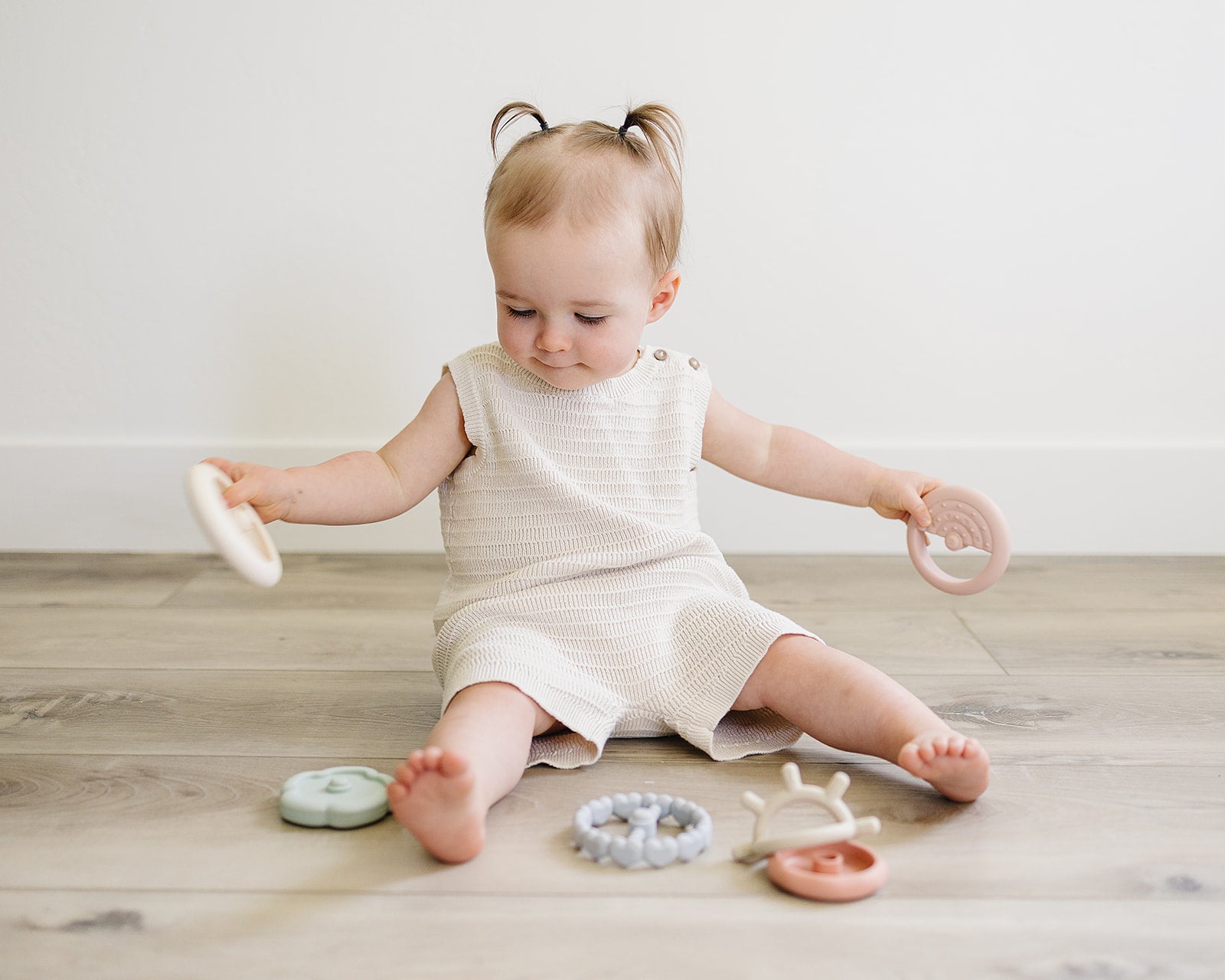 Young child sitting on a wooden floor with various teething toys around