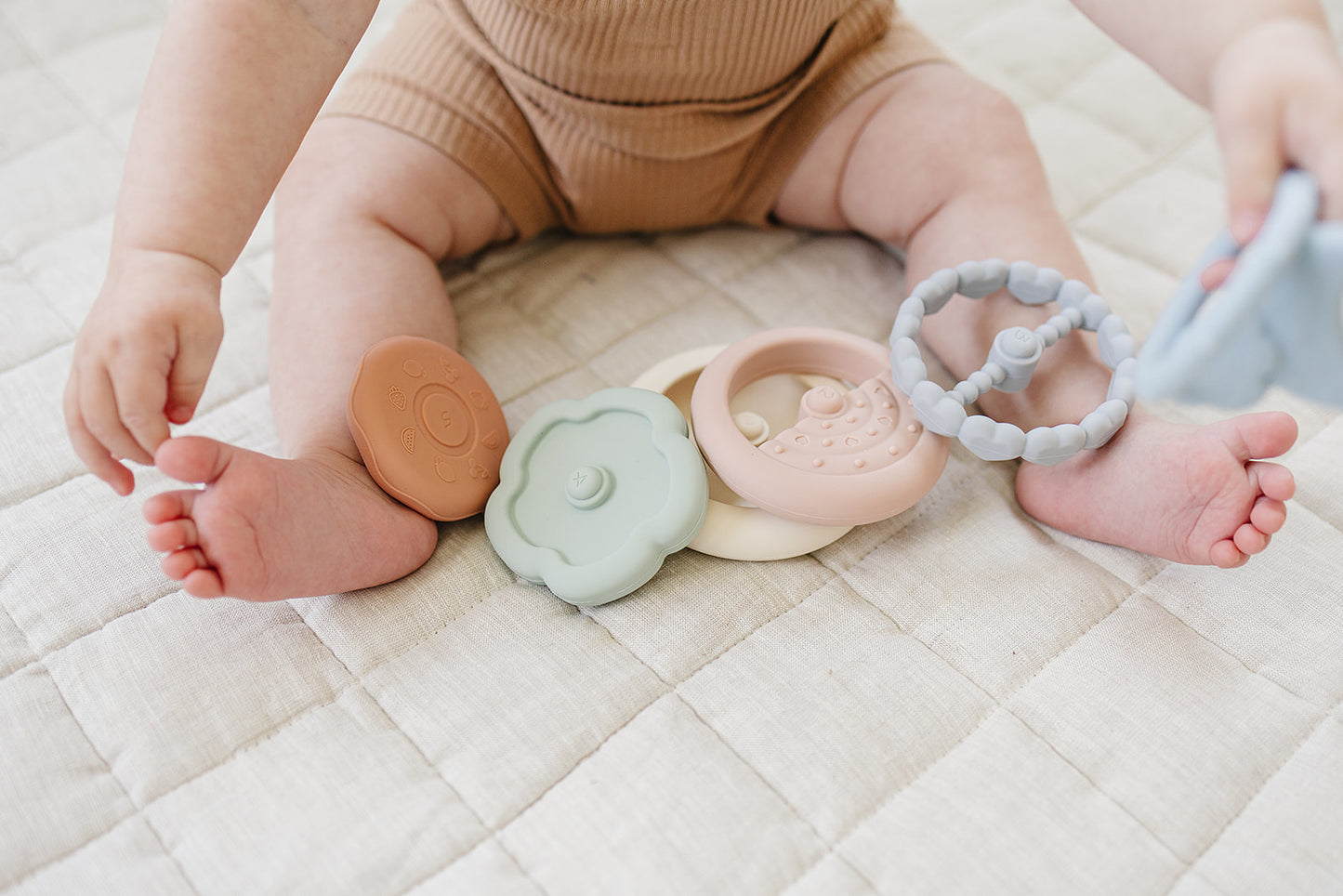 Baby's feet with colorful teething rings on a quilted surface