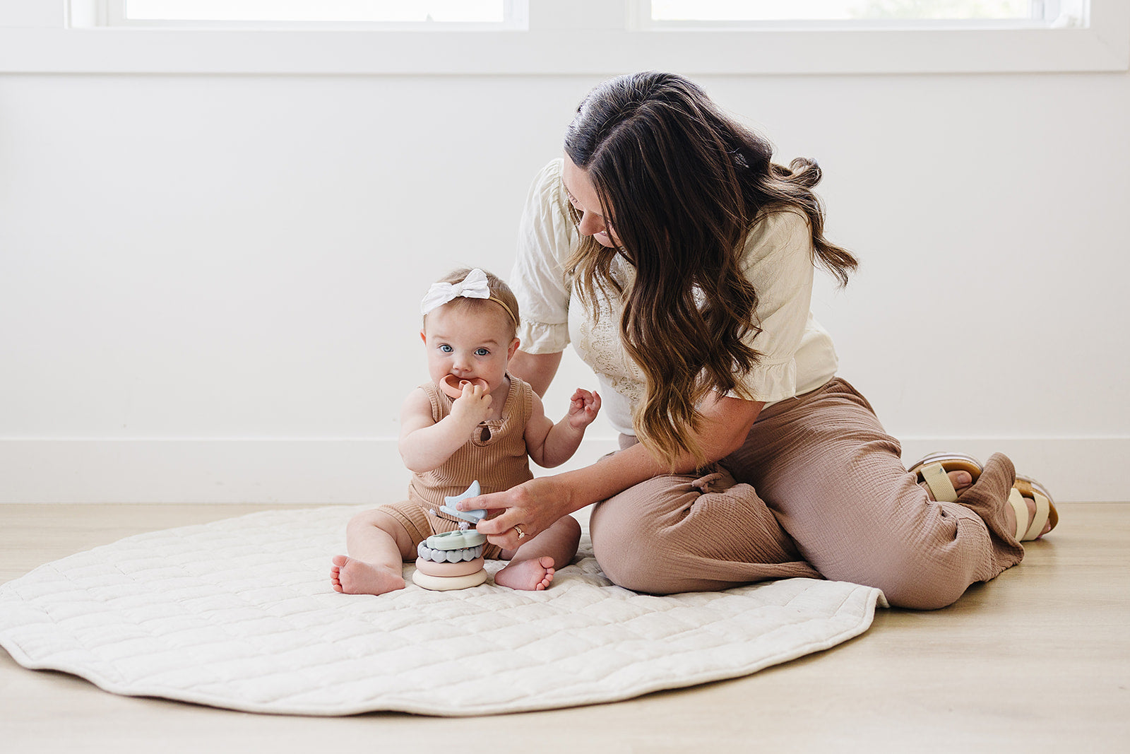 Woman and baby sitting on a white blanket in a bright room with silicon baby teether.  